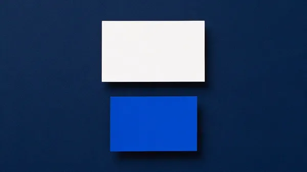 Una tarjeta de papel blanco y, debajo y separada, una tarjeta más chica de papel azul, sobre una superficie azul marino