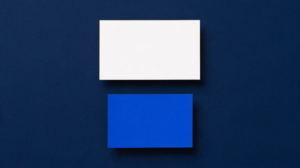 Una tarjeta de papel blanco y, debajo y separada, una tarjeta más chica de papel azul, sobre una superficie azul marino