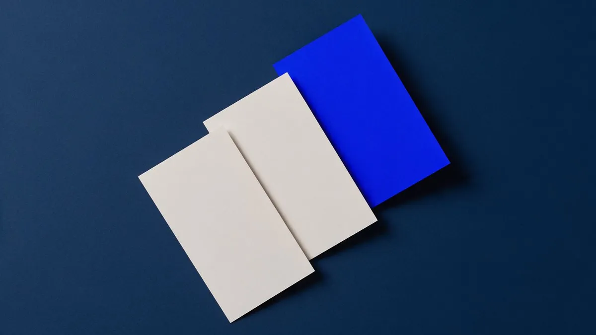 Tres tarjetas de papel que suben en escalón, dos blancas y la última azul, sobre una superficie azul marino