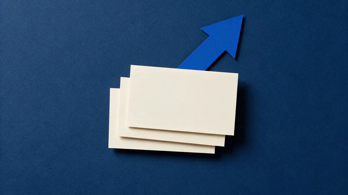 Tres tarjetas de papel crema idénticas apiladas en escalón y una flecha de papel azul subiendo por detrás, sobre una superficie azul marino