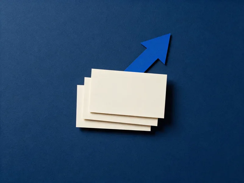 Tres tarjetas de papel crema idénticas apiladas en escalón y una flecha de papel azul subiendo por detrás, sobre una superficie azul marino