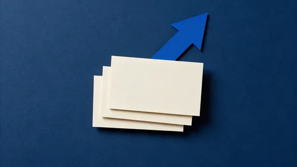 Tres tarjetas de papel crema idénticas apiladas en escalón y una flecha de papel azul subiendo por detrás, sobre una superficie azul marino