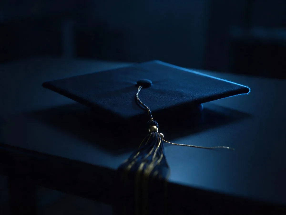 Un birrete de graduacion sobre un escritorio oscuro, iluminado de lado